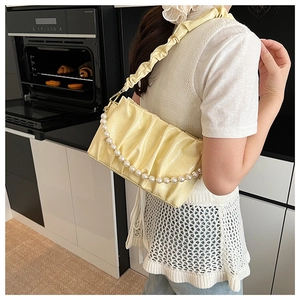 Close-up of bright yellow pleated cloud bag with elegant large pearl decorative chain
