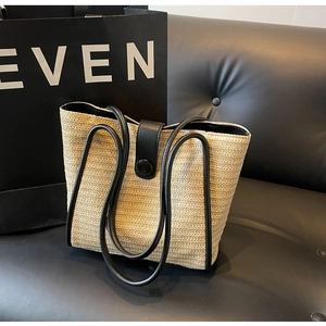 Detail of woven straw tote bag featuring black leather trim and secure button clasp