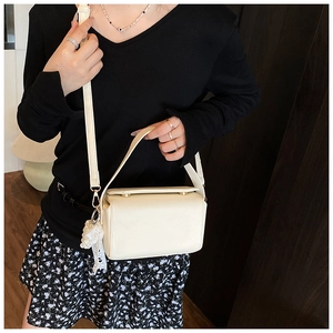 Detail of cream crossbody bag with textured faux leather and white lace pendant decoration