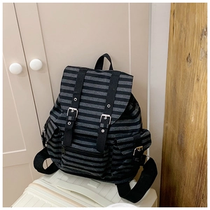 Detail of striped canvas backpack with leather straps placed on a white suitcase