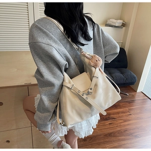 Detail of cream faux leather tote bag with wide eyelet strap and plush bear charm