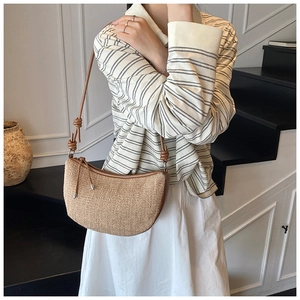 Detail of woven straw half-moon shoulder bag with brown leather strap and knot accent