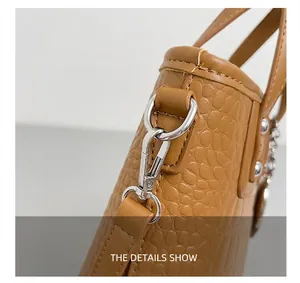 Close-up of silver metal hardware and crocodile texture on brown crossbody bucket bag