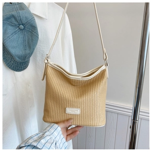 Close-up of beige woven straw shoulder bag with creamy leather strap and brand patch