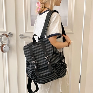 Side view of striped canvas backpack with leather straps and metal buckles on a model