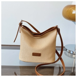 Detail of woven straw bucket bag with dark brown leather trim and silver hardware