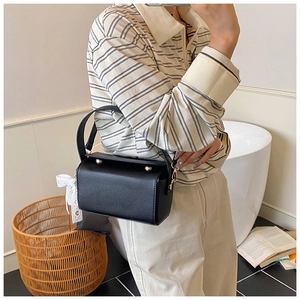 Side view of a black textured leather crossbody bag with a white lace bow charm