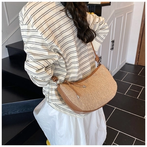 Detailed view of beige woven half-moon bag with brown leather trim and knotted strap details