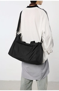 Grand sac de voyage en nylon noir porté en bandoulière dans un décor d'intérieur moderne
