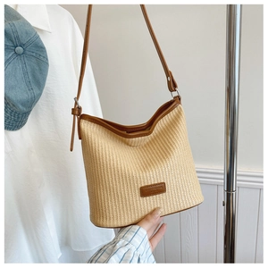 Detail of woven straw shoulder bag with brown leather strap and logo patch in casual setting