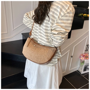 Detail of woven straw shoulder bag with brown leather trim worn by a model