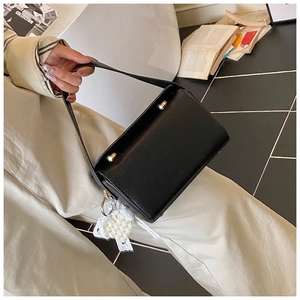 Detail of black pebbled leather crossbody bag with lace pearl charm and metal studs