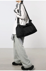 Détail d'un grand sac de voyage noir avec bandoulière réglable porté par un modèle