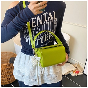 Close-up of bright green lychee leather crossbody bag with pearl heart charm accessory