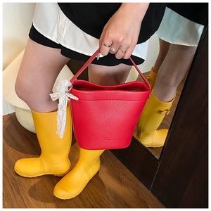 Dettaglio della borsa a secchiello in pelle rossa martellata con fiocco di pizzo bianco