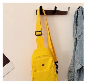 Detail of vibrant yellow canvas chest bag with adjustable black strap on wooden hook