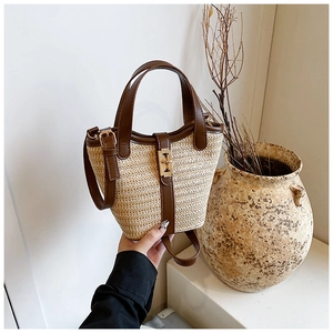 Detail of straw woven tote bag with brown leather trim and golden metal clasp closure