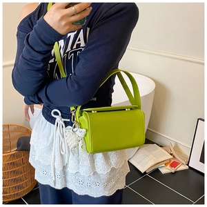 Detail of green lychee leather cylinder bag with pearl bow pendant and metal accents