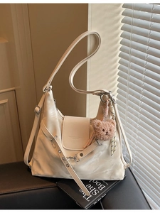 Minimalist beige hobo bag with teddy charm and adjustable strap on a side view