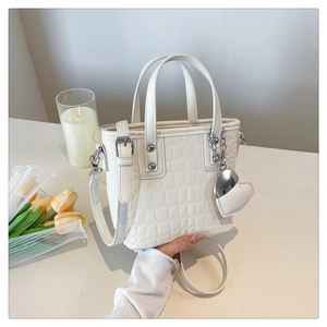 Detail of creamy white crossbody bucket bag with crocodile pattern and heart charm