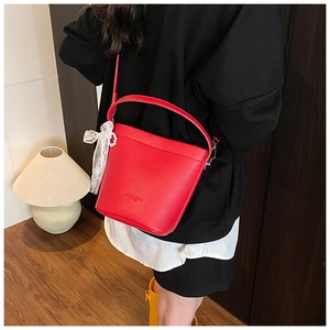 Dettaglio di una borsa a secchiello in pelle rossa con fiocco in pizzo e ciondolo di perla