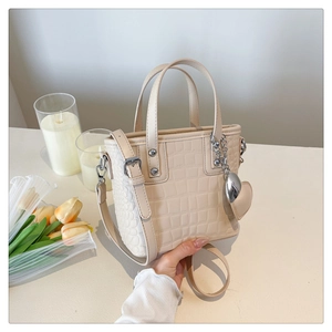 Detail view of beige crocodile pattern bucket bag with silver heart charm and chain link