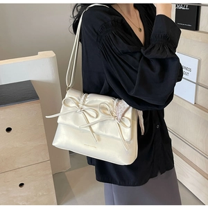 Détail du sac crème avec nœud papillon, foulard en soie et rabat plissé élégant