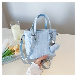 Detail of light blue crocodile embossed crossbody bucket bag with heart pendant charm