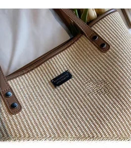 Detail of woven straw tote bag featuring brown leather handles and premium metal rivets