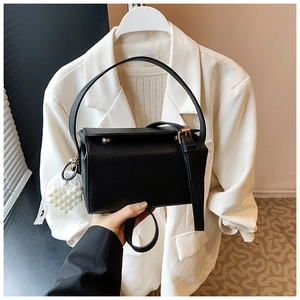 Detail of black litchi texture leather handbag with gold hardware and pearl heart charm