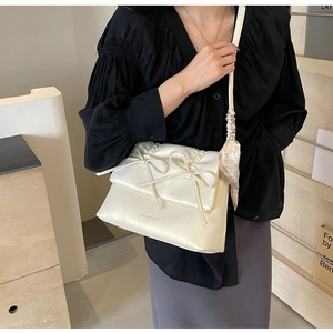 Détail du sac crème avec nœuds, logo doré et foulard en soie à motifs de cœurs