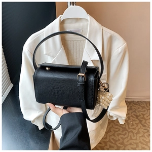 Detail of black lychee leather handbag with gold buckle and elegant pearl pendant accessory