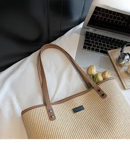 Detail of woven straw tote with brown leather straps and black metal logo on desk