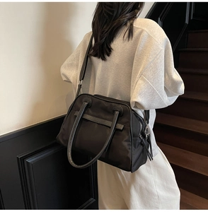 Vista posteriore di una modella con una grande borsa da viaggio in nylon nero e manici in pelle