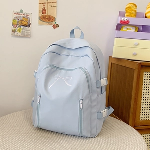 Détail du sac à dos bleu clair en tissu avec broderie de nœud blanc et poches zippées