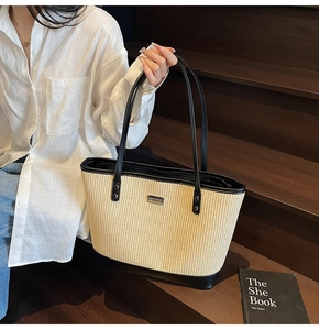 Detail of light beige woven tote bag with black leather trim on wooden stairs