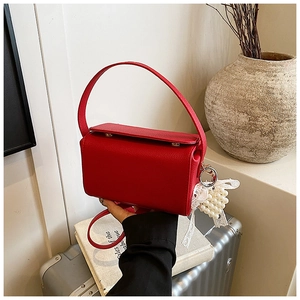 Detail of red faux leather handbag with lychee texture and pearl bow charm accessory