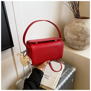 Detailed view of red lychee grain leather handbag with pearl charm on a metallic suitcase