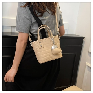 Detail of beige crocodile embossed bucket bag with a heart-shaped charm and long strap