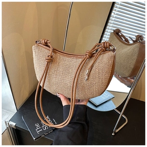 Close-up of woven straw crescent bag with brown leather trim and knotted strap detail