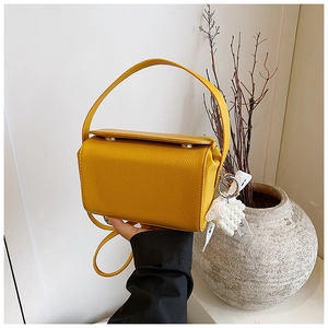 Detail of yellow pebbled leather crossbody bag with pearl lace bow charm and silver hardware