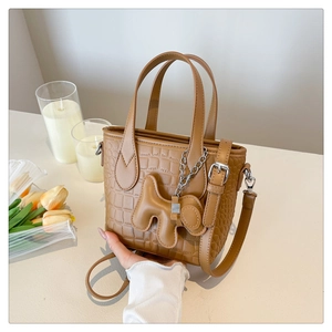 Close-up of brown crocodile texture bucket bag with a cute dog-shaped charm on a table