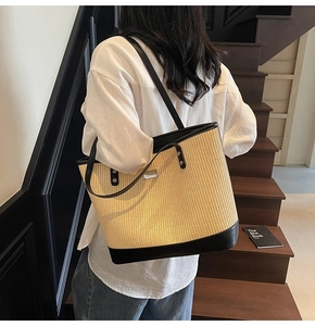 Detail of a woven straw tote bag with black leather straps worn over a white shirt