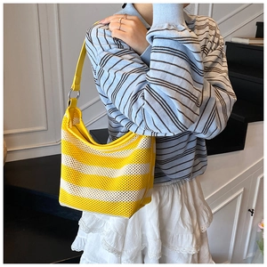 Close-up of woven striped tote bag with yellow leather strap on model's shoulder