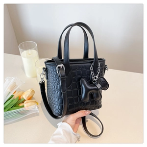 Detail of crocodile embossed crossbody bag featuring a playful dog charm and shoulder strap