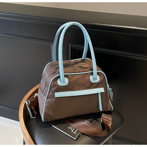 Dettaglio dei manici in pelle blu e cerniera su borsa da viaggio in nylon marrone su sedia