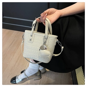 Detail of cream mini bucket bag with crocodile texture and heart charm in model's hand