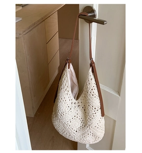 Macro detail of beige crochet hobo bag with brown leather strap hanging on a door