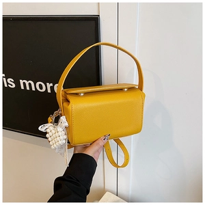Close-up of bright yellow crossbody bag with lychee leather texture and pearl heart charm