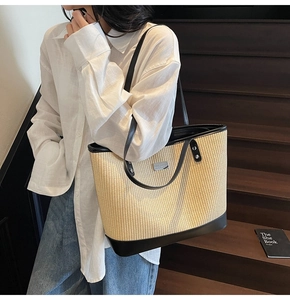 Close-up of beige woven tote bag with black leather straps and silver metal logo on stairs